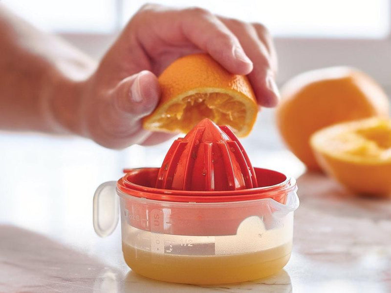 orange fruit being juiced using the tupperware all in one mate red juicer with oranges in background