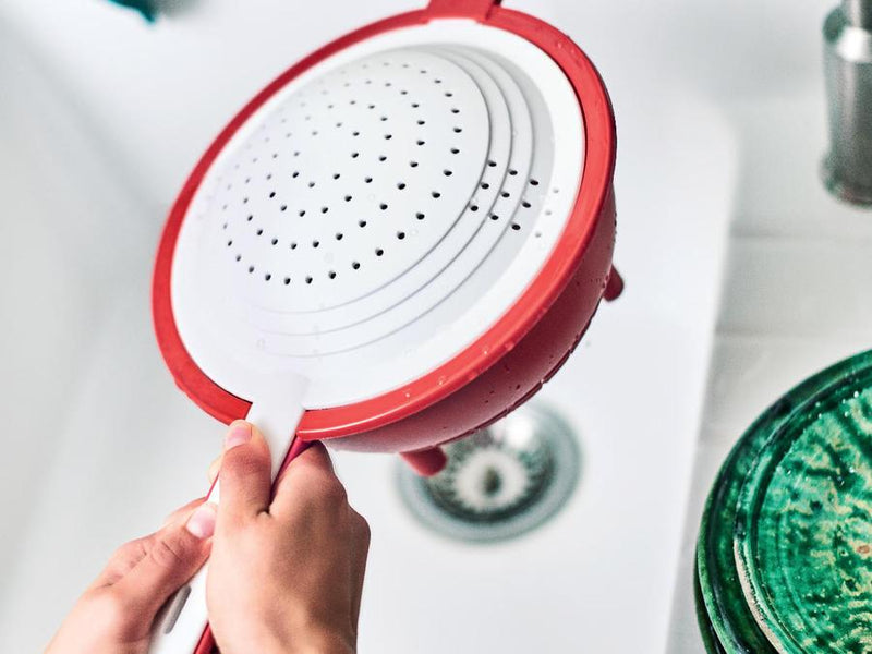 woman holding tupperware double colander over kitchen sink