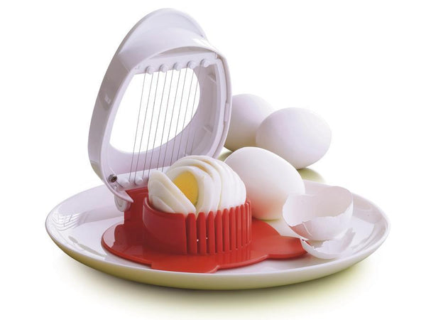 Tupperware Red and Gray Egg Slicer on a white plate with eggs in the slicer and cracked egg shells on the right of the egg slicer