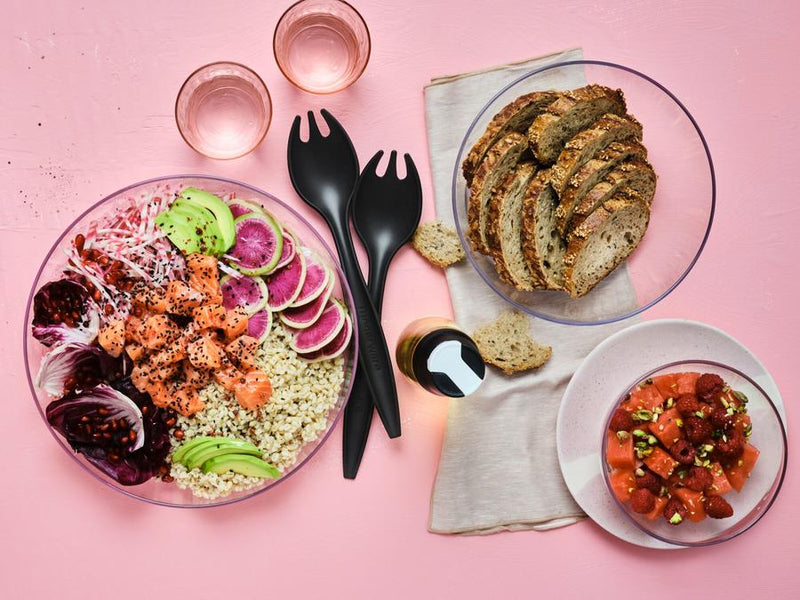 two black tupperware serving forks sitting between bread and poke bowl